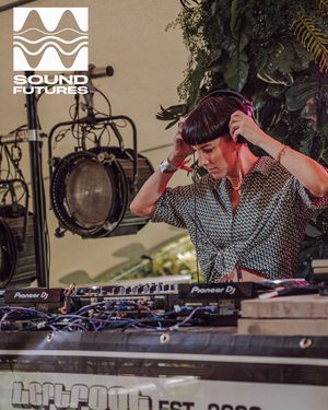 A DJ stand in front of her equipment, holding headphones