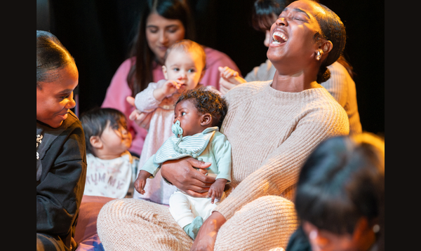 A lady is laughing whilst holding her baby. There are other families in the background.