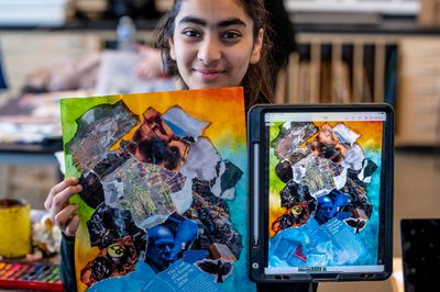 Young person holds up zine with artwork and digital zine on an iPad smiling.