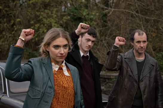 Two men and one woman (Imogen Poots) in 1970s clothing hold their fists up.