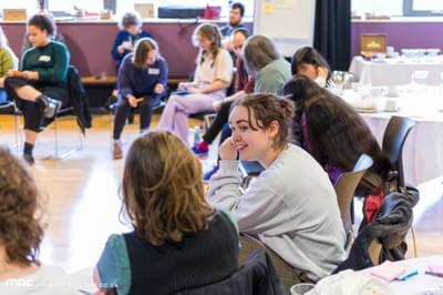 Two women chatting in a large room with other people talking in the background