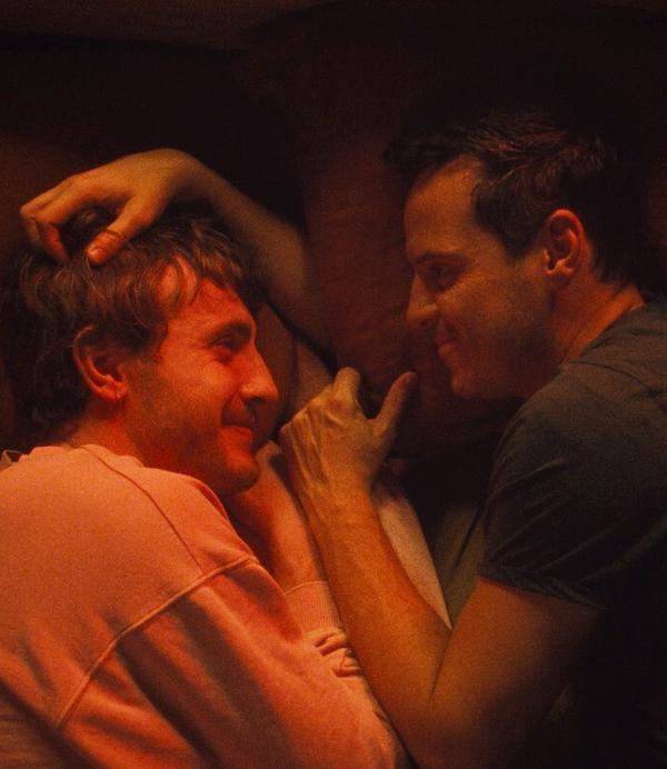 Two men (Paul Mescal and Andrew Scott) face each other lying in bed with their arms touching.