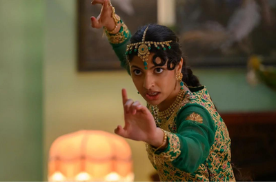 A young Asian woman wearing a decorative headpiece, jewellery and a a green and gold outfit holds out her arms in a martial arts pose.