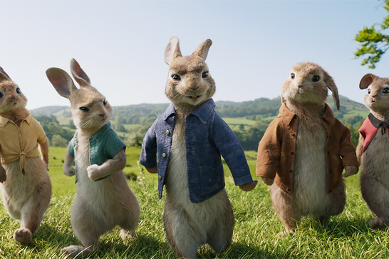 Five animated rabbits wearing different coloured jackets walk forwards on their back legs like humans, in a grassy and hilly landscape.