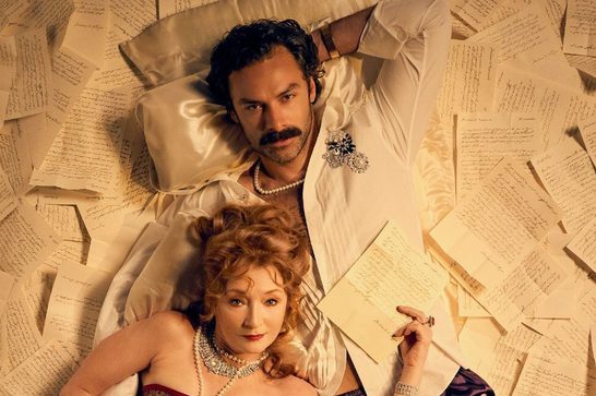 The image shows two elegantly dressed figures in Regency or Victorian-era costumes, photographed from above while lying among scattered handwritten letters and papers. The styling suggests a romantic narrative, with both wearing formal period attire and jewelry including pearl necklaces. The man wears a white formal suit while the woman wears what appears to be an evening gown with elaborate jewelry.