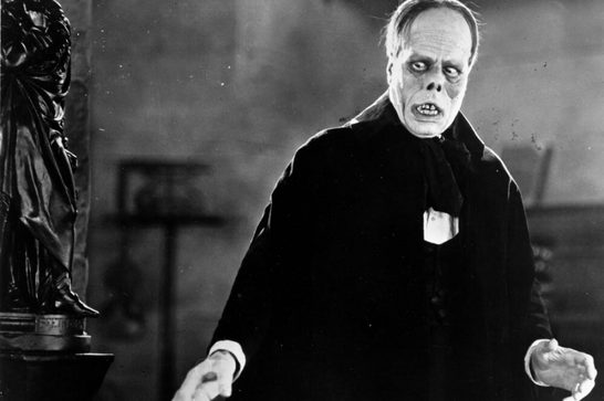 A striking still from "The Phantom of the Opera" (1925), one of the most iconic silent horror films. The image captures Lon Chaney Sr. in his legendary portrayal of Erik, the Phantom, showcasing the dramatic makeup and prosthetics that made this performance revolutionary for its time. Chaney, known as "The Man of a Thousand Faces," designed much of his own makeup for the role, creating the Phantom's skull-like appearance with sunken features, exposed teeth, and an upturned nose.