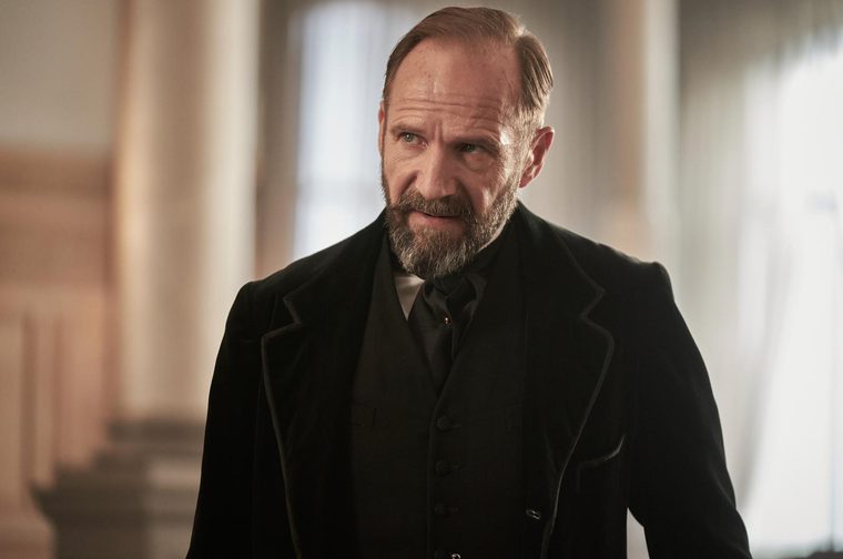 We see a distinguished-looking man in period costume - specifically early 20th century, with a formal black suit and cravat.