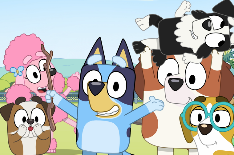 A group of animated cartoon dog characters from the children's TV show Bluey, gathered together in a park setting. In the centre is Bluey, a blue and tan heeler puppy with arms outstretched and a big smile. To the left is a pink poodle character holding a stick, standing behind a small brown and white bulldog puppy. To the right is a larger brown and white dog carrying a black and white puppy on its shoulders. In the front right is a small yellow and white dog wearing teal-framed glasses. The background shows green hills, trees, and a fence under a light blue sky.