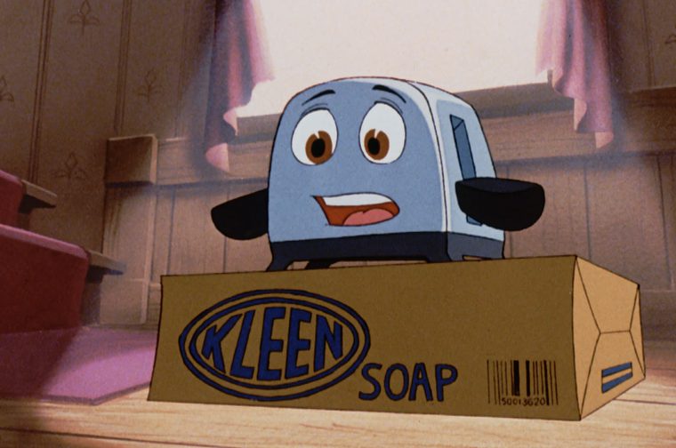An animated toaster character with expressive eyes and a surprised smile is standing on a cardboard box labeled 'Kleen Soap,' in a cozy wood-paneled room with a staircase and pink curtains in the background.