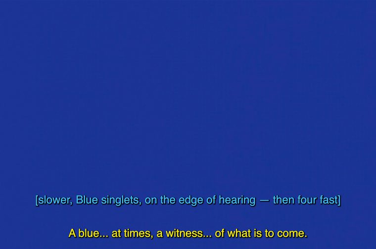 A solid blue image featuring subtitles in a lighter blue saying 'slower, blue singlets, on the edge of hearing - then four fast.' Below are yellow subtitles saying 'A blue...at times, a witness...of what is to come.'