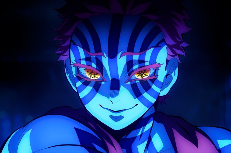 A close-up shot from the anime 'Demon Slayer' showing a demon character with distinctive blue and purple striped markings across their face and body. The character has spiky dark hair and glowing golden/yellow eyes with red markings around them. Their skin appears pale blue-tinted, and they're wearing dark clothing. The background is a deep blue with atmospheric lighting effects. The character has a menacing smile, emphasizing their supernatural, demonic nature. The art style is typical of the Demon Slayer anime series with bold colours and dramatic lighting.