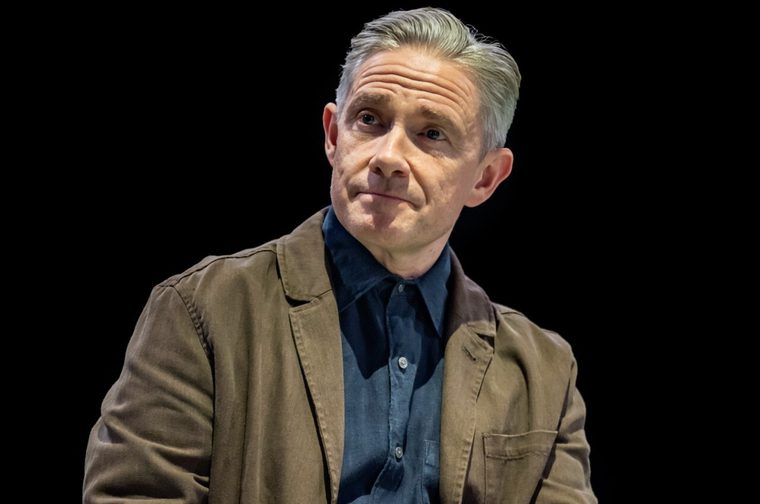A man in his fifties (Martin Freeman) with grey hair looks off to the left of the frame. He is wearing a blue denim shirt and a light brown jacket.