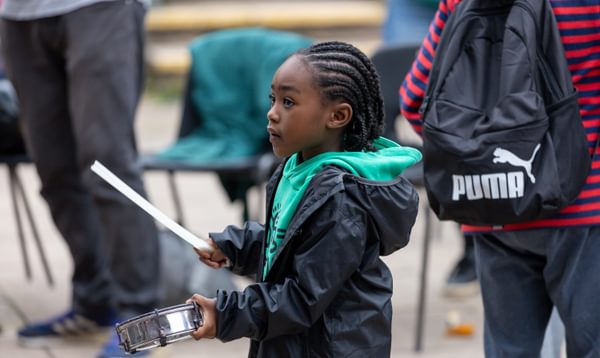Young boy in a green jumper holds a drumstick looking away from the camera