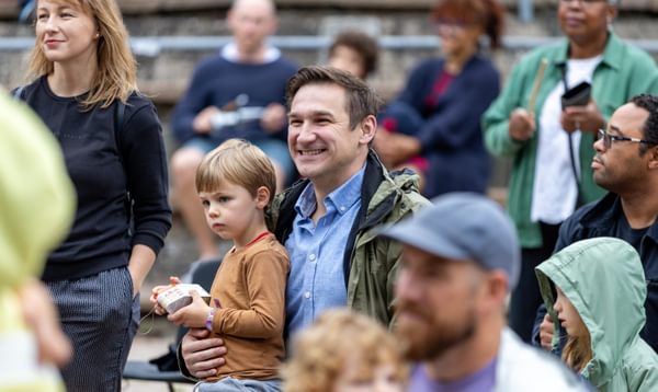 Man and his young son smiling outside surrounded by a crowd of people watching a show not captured in the picture