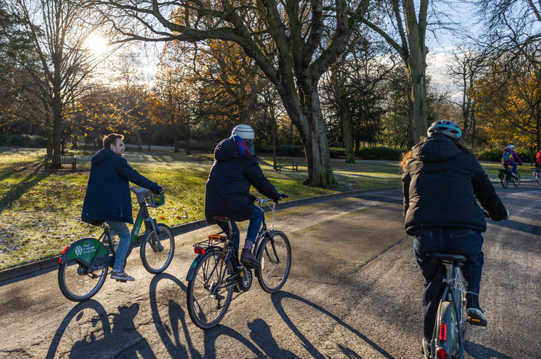 Three people cycling through a park on a sunny but wintery afternoon.