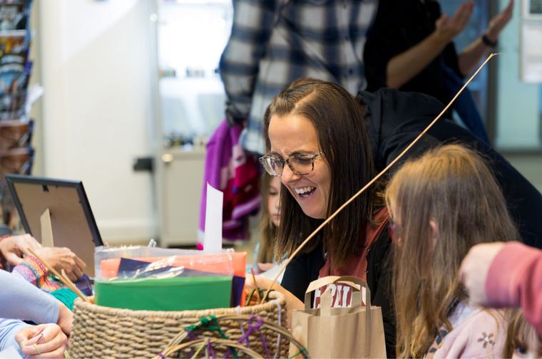 A parent with long brown hair and glasses sat down at a crafting table with two children either side.