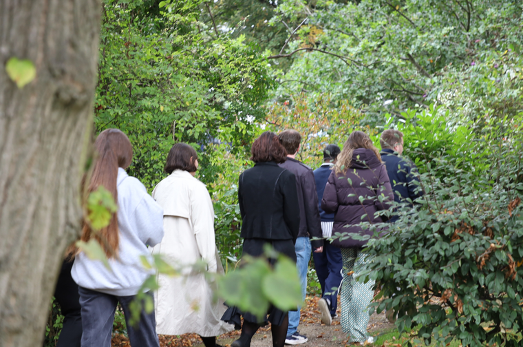 A group of people walk through a park, surrounded by trees and greenery.