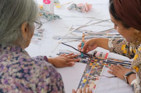 Older woman takes part in weaving workshop with younger woman