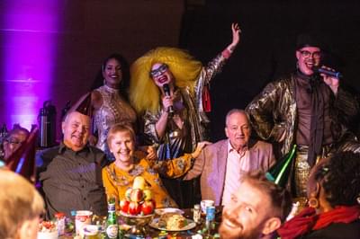 Group of smiling seniors at a party table with drag artist