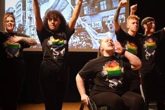 Group of young people with rainbow tshirts on performing in front of a film projection