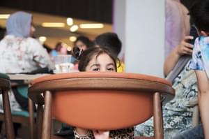 Young girl peeks face above chair in MAC's café