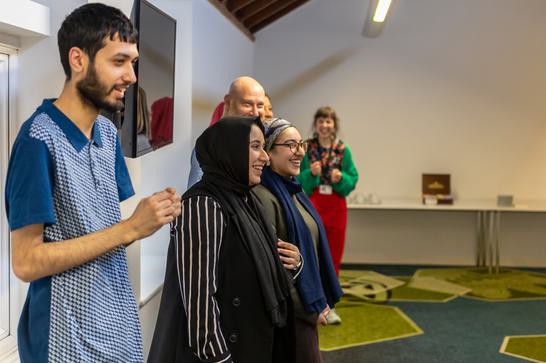 Multi-cultural and diverse group stood in a room smiling faced away from the camera