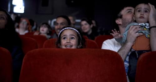 A young girl smiling in a cinema, next to a man holding a wide-eyed baby