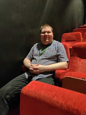 Man sits in cinema seat smiling at the camera