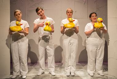 Four performers dressed all in white holding big yellow rubber ducks