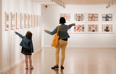 A woman and a little girl point at photography on bright white gallery walls