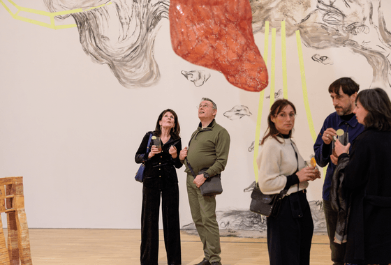 A woman and a man stand in an art gallery looking up at a red sculpture