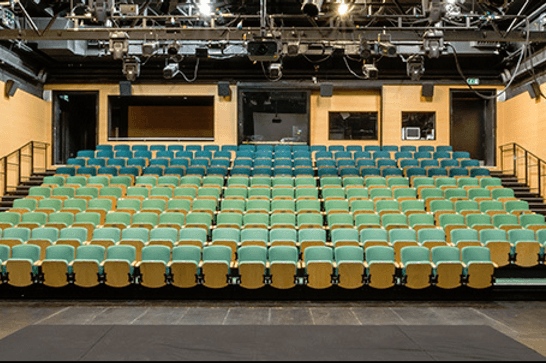 View from the stage of MAC's main theatre, oak coloured walls and rows of turquoise seats