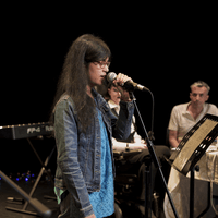 A woman with dark hair and glasses singing into a microphone