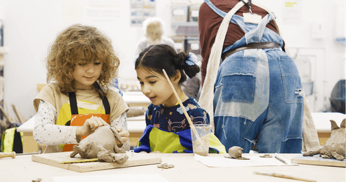 Two smiling children create a pottery sculpture in studio