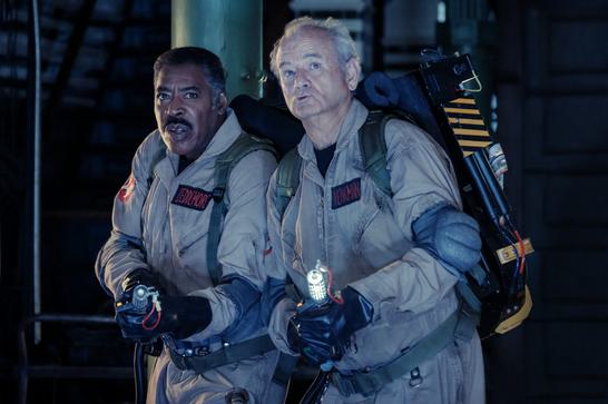 Veteran Ghostbusters Ernie Hudson and Bill Murray hold proton packs as they look up off camera.