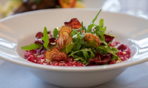 A dish of beetroot risotto is the main focus of this image, and it has been beautifully garnished with salad