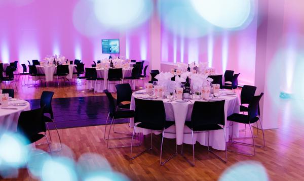 Tables can be seen through white twinkling lights, and the room has a pink hue to it.