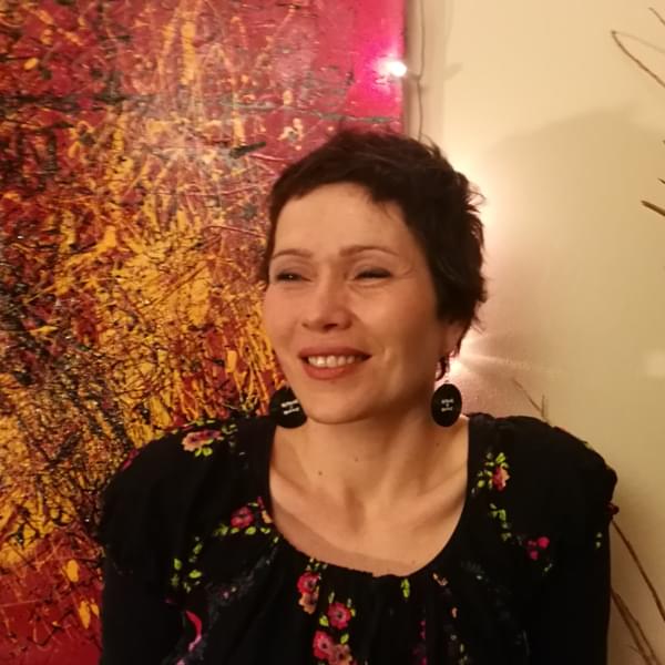 ILdiko has short brown hair and is wearing a floral top and circular earrings.