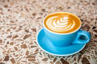A blue coffee mug on a speckled brown table, with latte art forming a flower