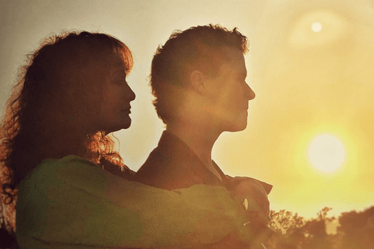 A women embraces the man in front of her as they look at a sunset.