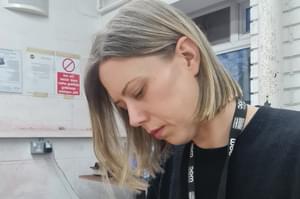 Chloe has light blond hair down to her shoulders, and is sat at a table filing down metal jewellery