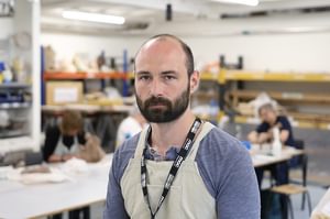 Martin has a beard, is wearing a blue top and apron and is in a ceramic studio