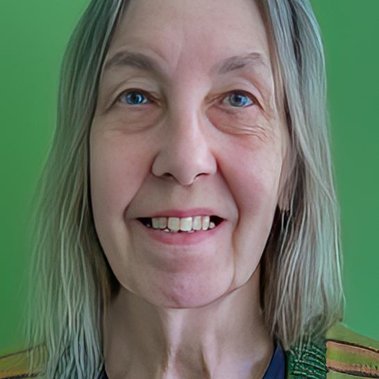 Sue has long grey hair, is smiling and is standing against a bright green background.