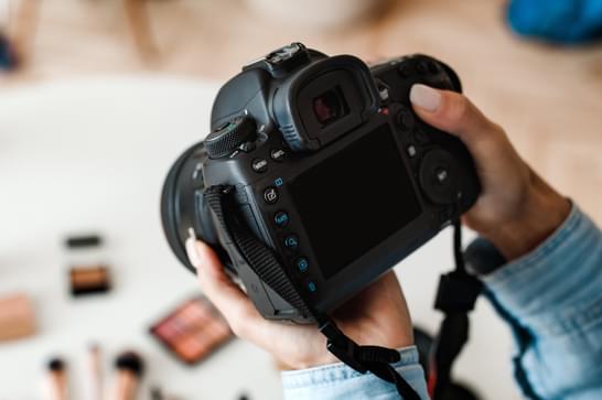 A close up shot of a hand holding a camera, aiming it at blurred objects in the background.