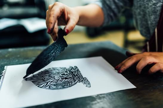A person is lifting up a lino cutting from a piece of paper, leaving a floral print on the white paper
