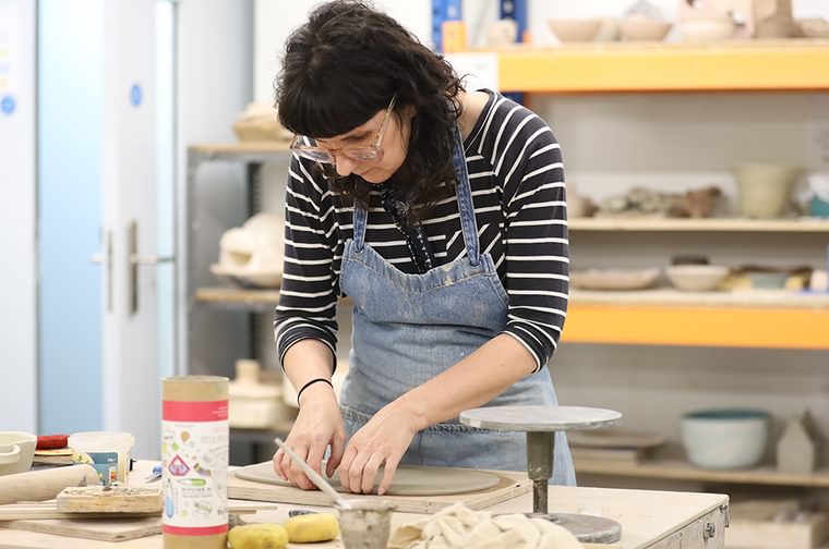 A woman is rolling our clay on a table