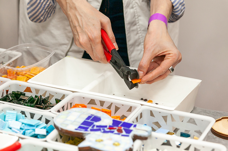 A person is cutting an orange tile, surrounded by different coloured cut tiles