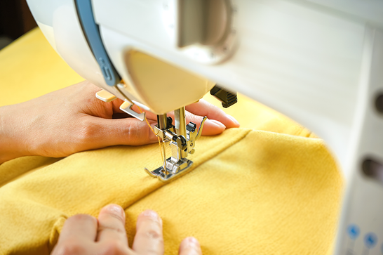A persons hands is guiding yellow fabric through a white sewing machine