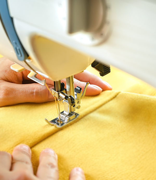 A persons hands is guiding yellow fabric through a white sewing machine