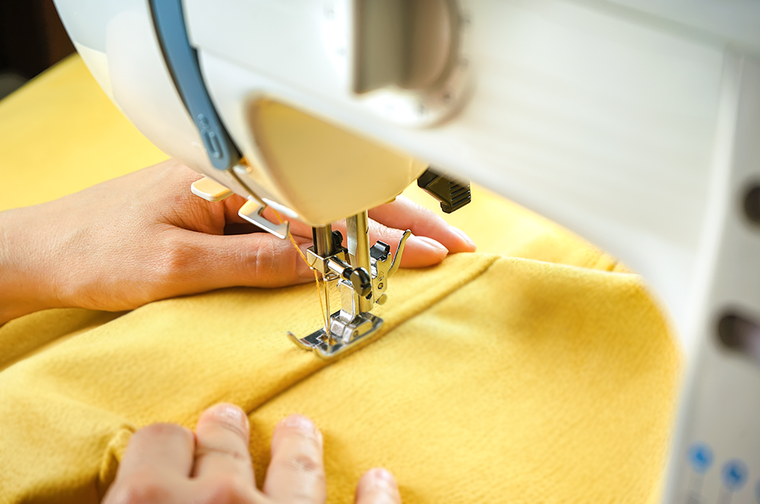 A persons hands is guiding yellow fabric through a white sewing machine
